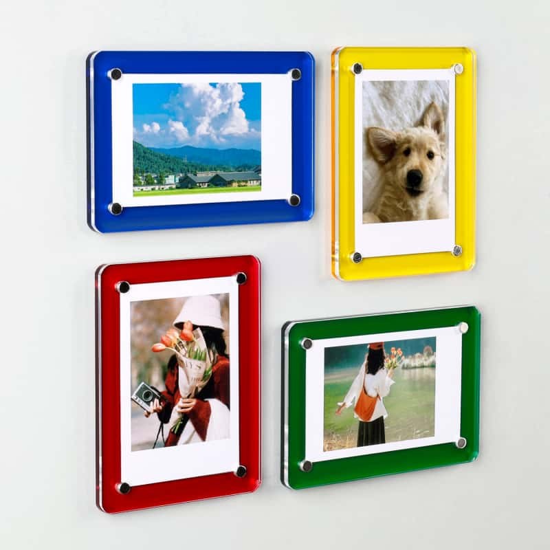 Four acrylic magnetic picture frames in blue, yellow, red and green mounted on a pale wall, each with a photo held by four corner magnets