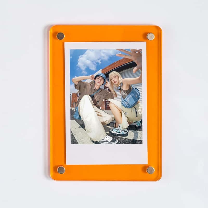 An orange acrylic magnetic picture frame holding a group photo, mounted on a white wall