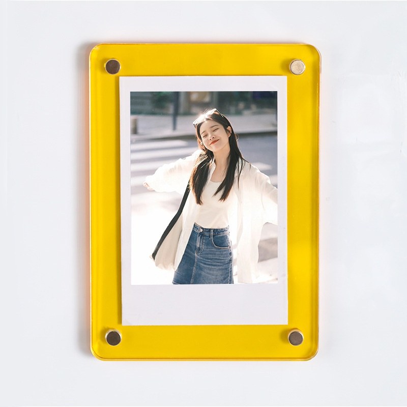 A yellow acrylic magnetic picture frame holding a 3-inch instant photo, mounted on a white wall