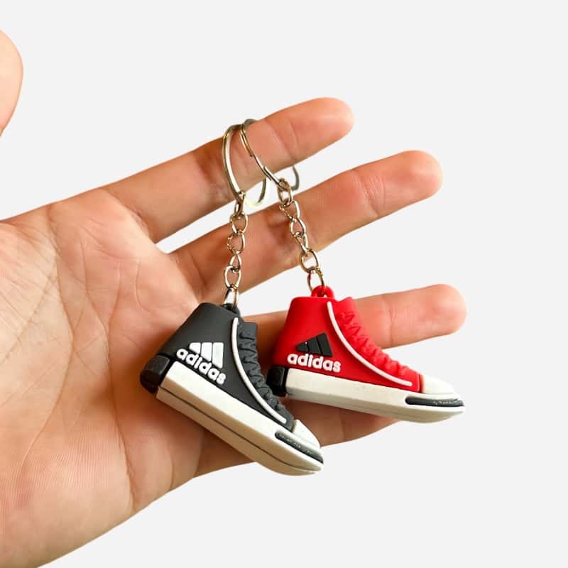 Adidas mini shoe keychains in black and red held in one hand, showing the laces, eyelets and moulded sole