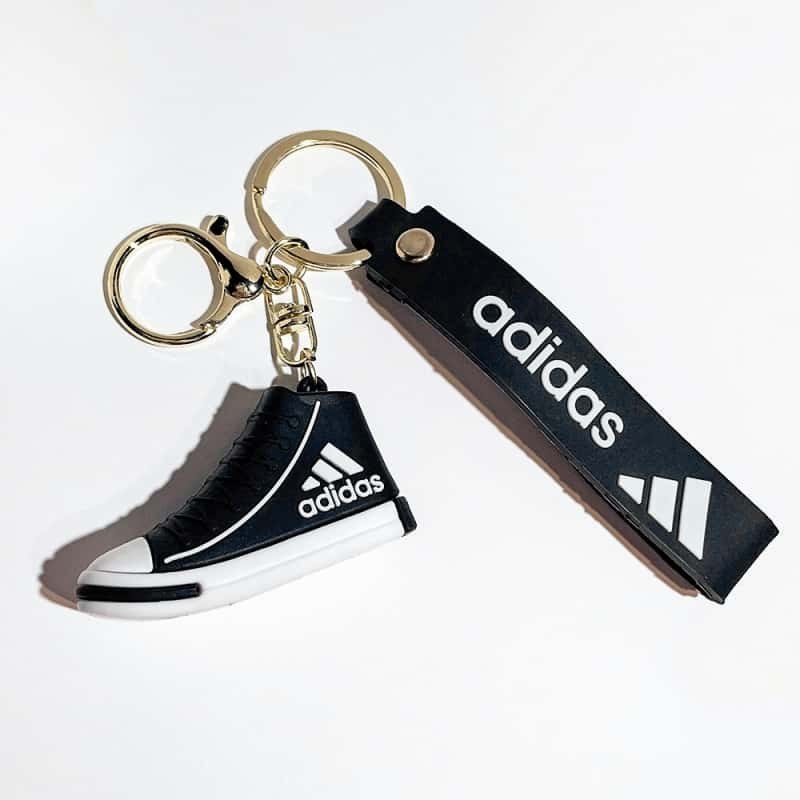 Adidas mini shoe keychain in black, with a black printed wrist strap and gold-tone split ring and clasp