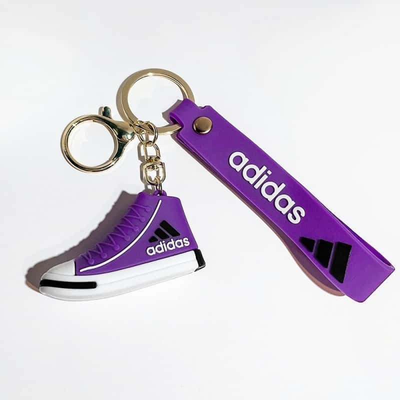Adidas mini shoe keychain in purple, with a matching printed wrist strap and gold-tone split ring on a short chain