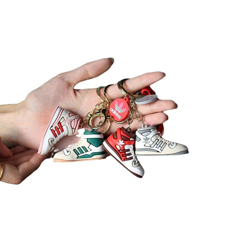 Adidas shoe keychains in red, green, white and cream held on one hand, shown as a shape and shade reference