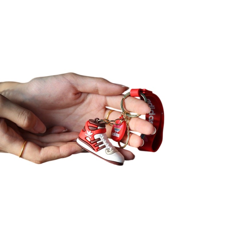 Adidas shoe keychain in red held in the palm, showing the tag strap, the disc charm and the split ring