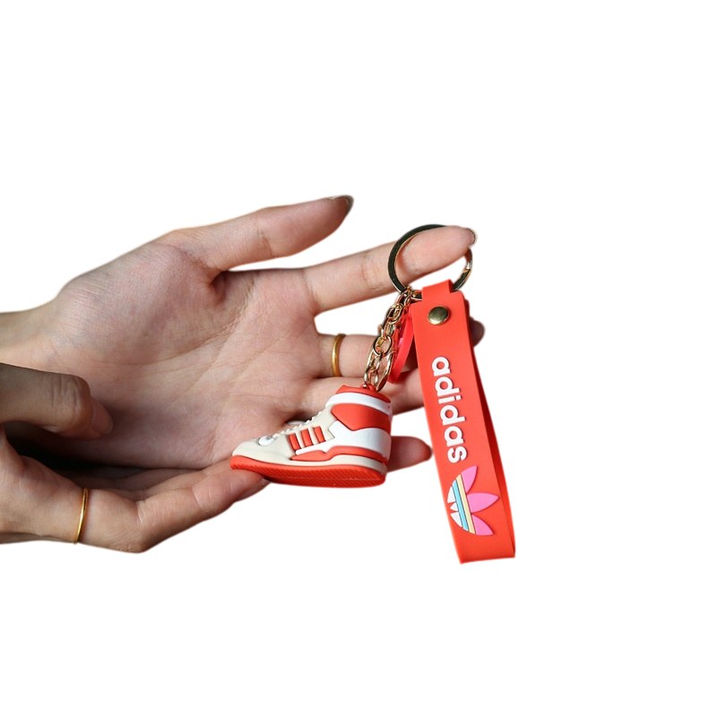 Adidas shoe keychain close up: the red tag strap, the round disc charm and the gold-tone split ring