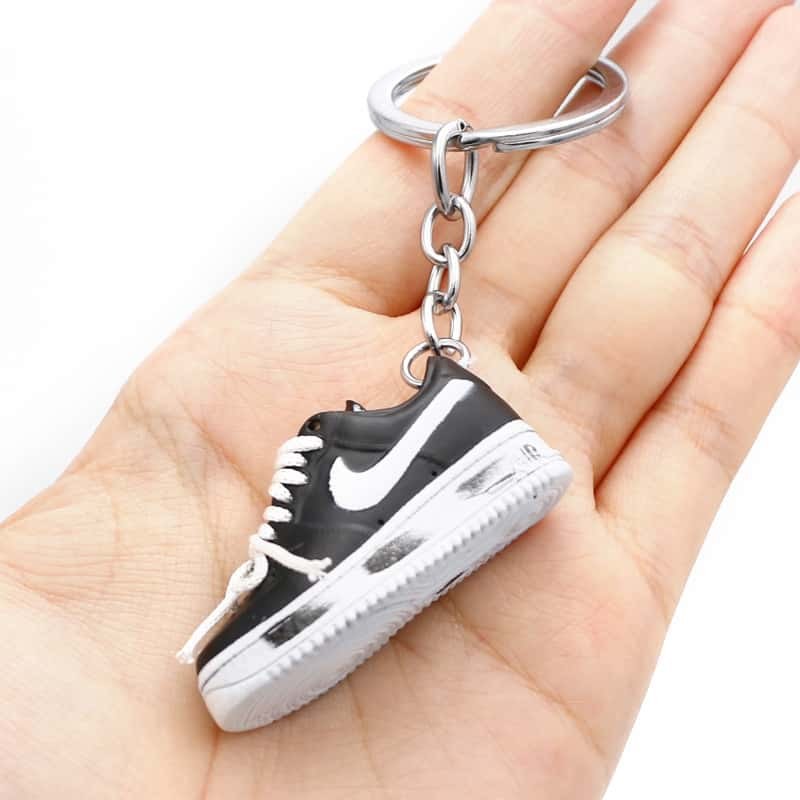 Air Force One shoe keychain in black PVC held in one hand, showing the low-top profile and flat moulded sole