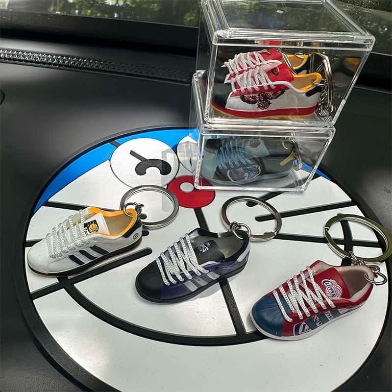 Basketball shoe keychains arranged on a round court-patterned tray beside a clear case holding a pair