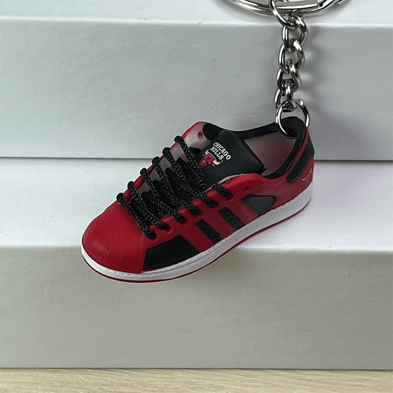 Basketball shoe keychain in red and black hanging from its keyring against a plain background