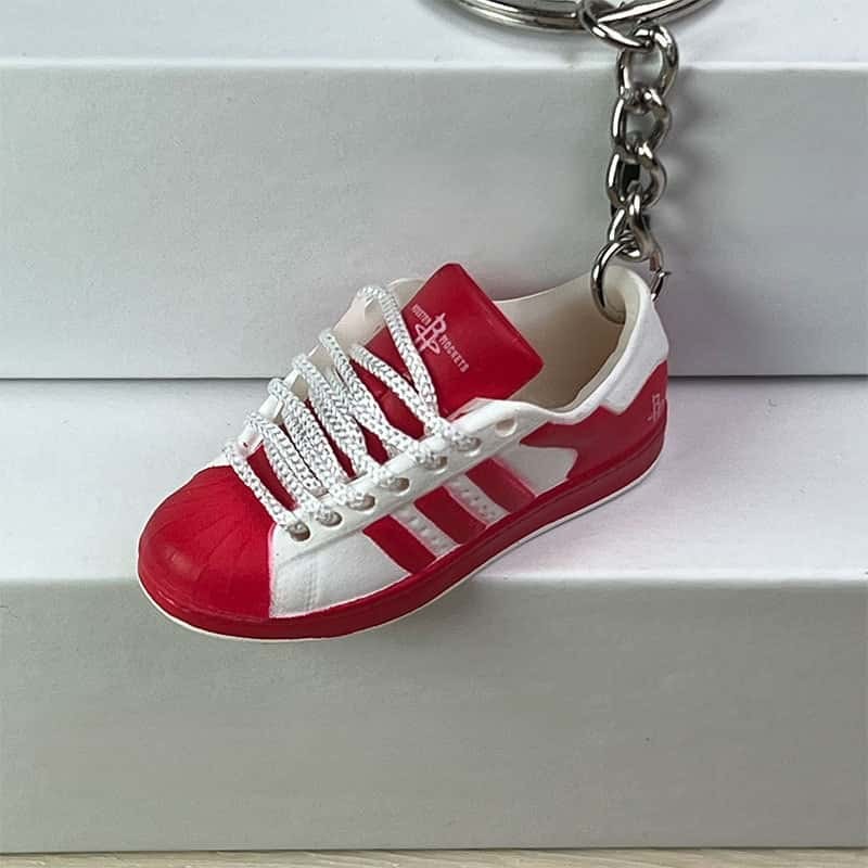 Basketball shoe keychain in white and red hanging against a white step, showing the chain and split ring