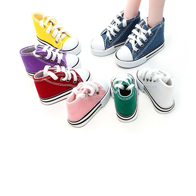 Canvas shoe keychains in assorted colors placed beside a real foot to show how small they are