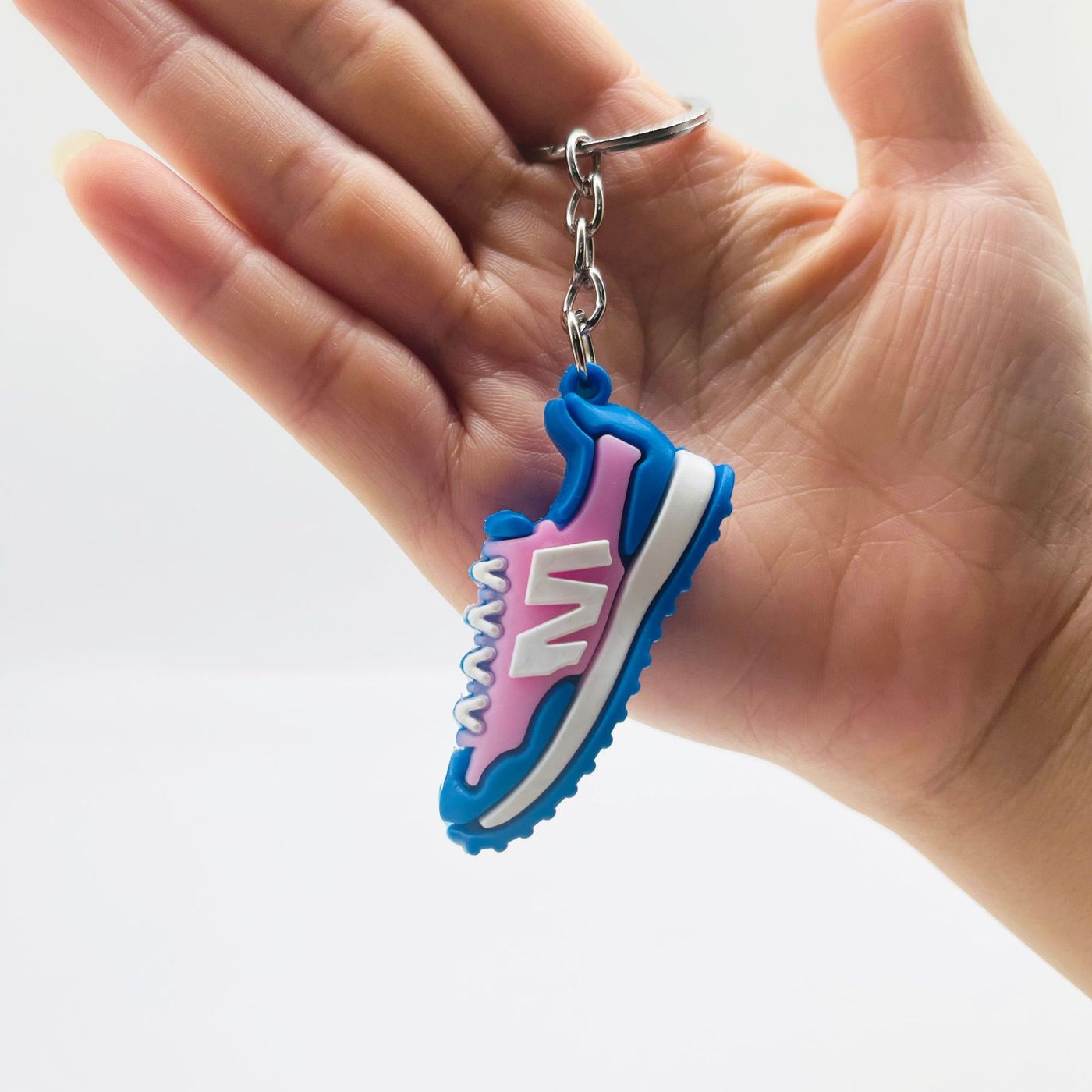 Pink and blue PVC sneaker keychain held in a hand, showing the two-tone upper