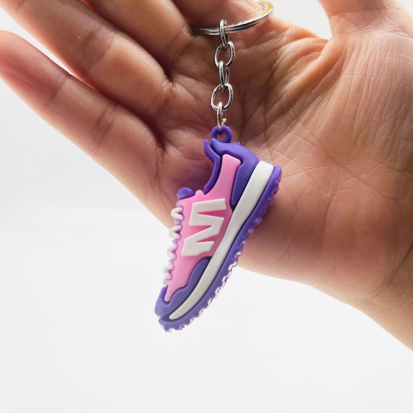Pink and purple PVC sneaker keychain with the molded letter M, held in a hand
