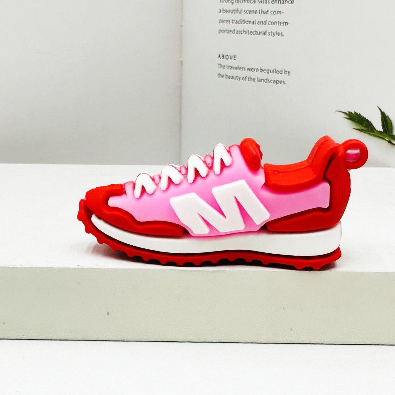 PVC sneaker keychain photographed on a display block with a book and dried flowers
