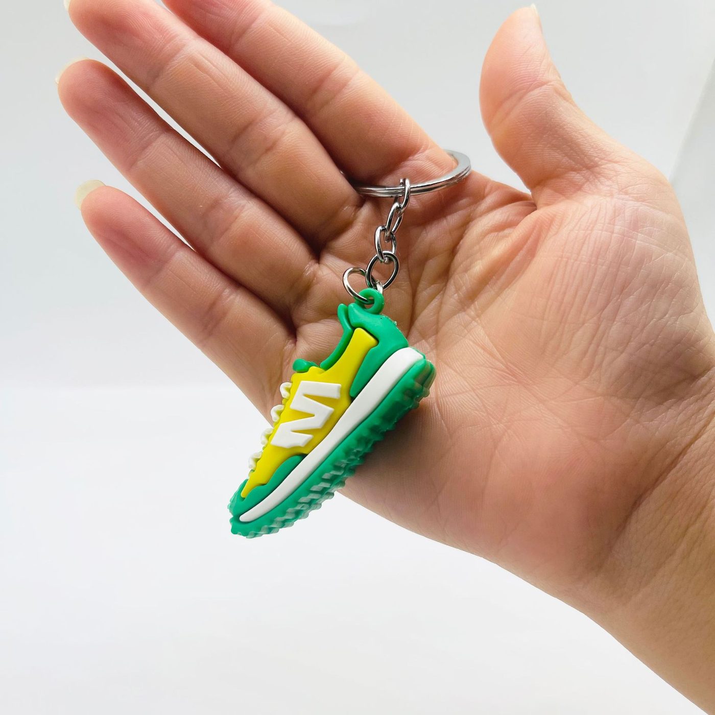 Yellow and green PVC sneaker keychain held in a hand, showing the sidewall