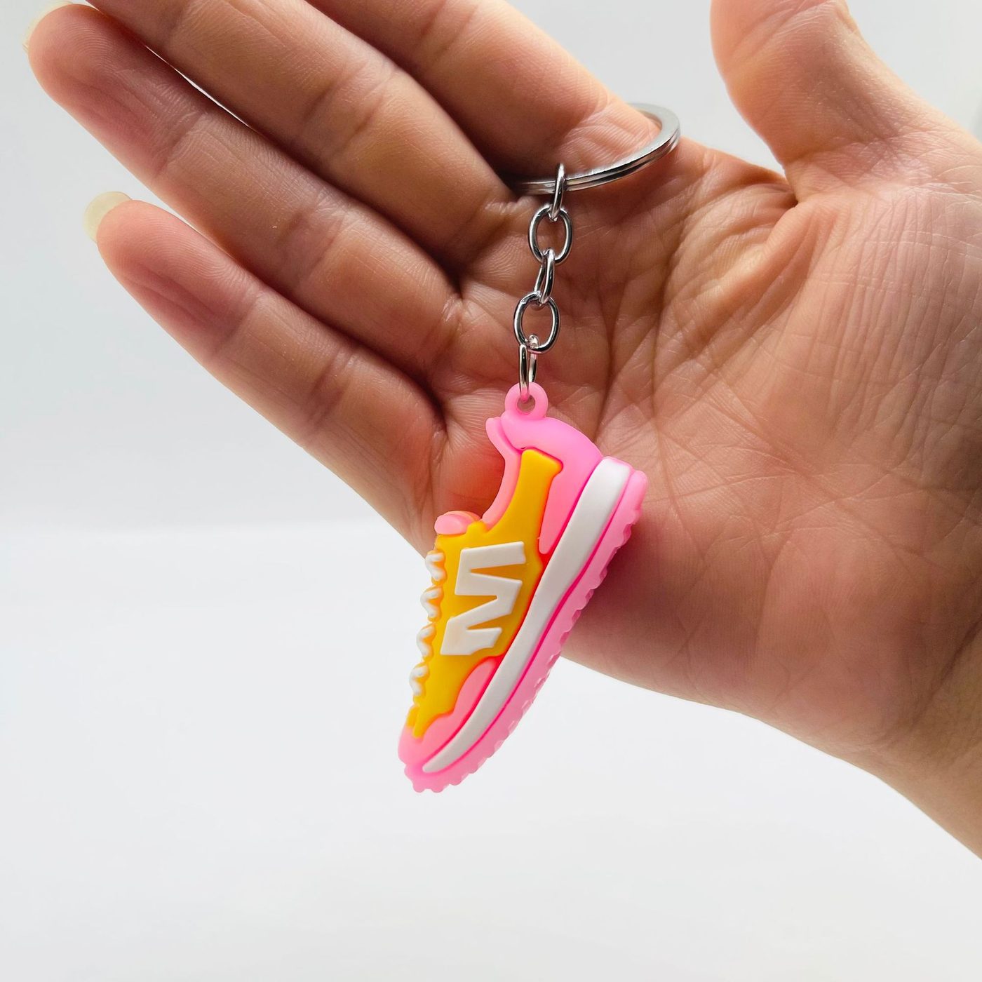 Yellow and pink PVC sneaker keychain held in a hand, showing the molded laces