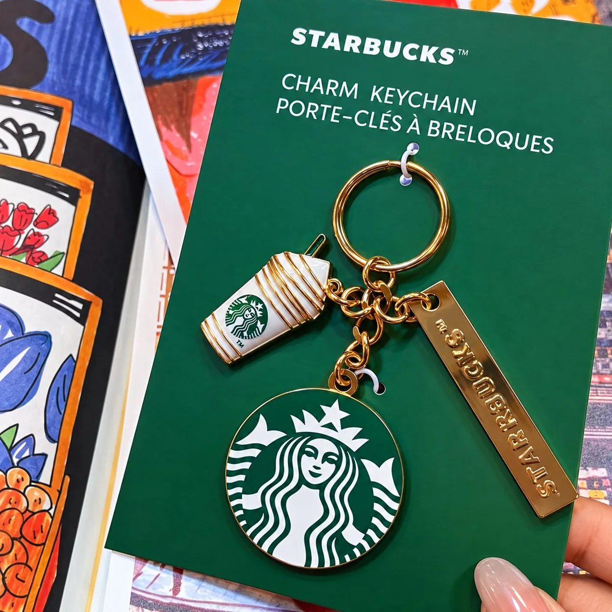 Starbucks-style branded bag charm — a miniature coffee-cup charm paired with a green enamel pendant and an engraved name plate on a polished gold-tone ring.