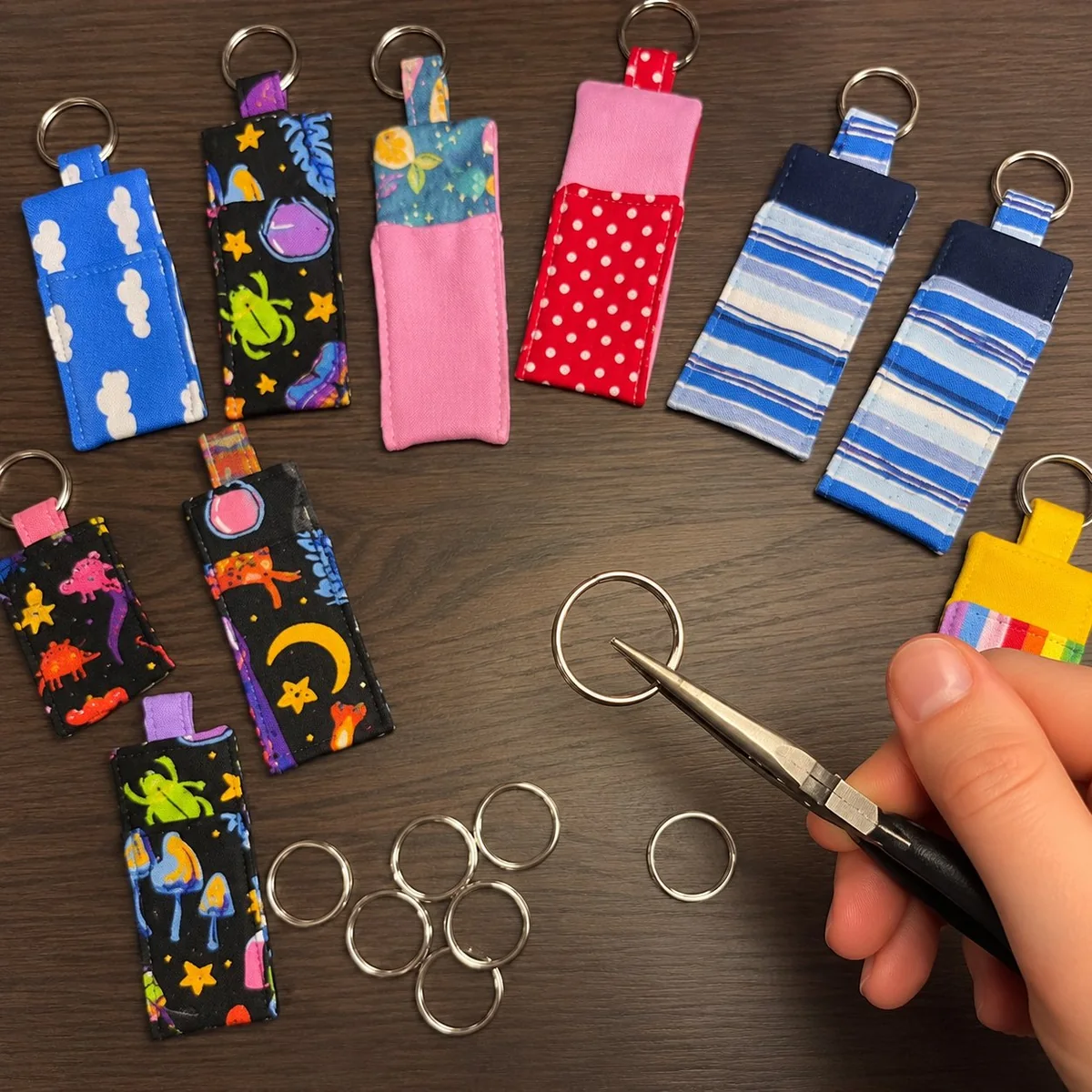 A pair of flat-nose pliers resting beside a small set of fabric keychains with split rings and lobster clasps — the standard setup for attaching or adjusting charms on bags