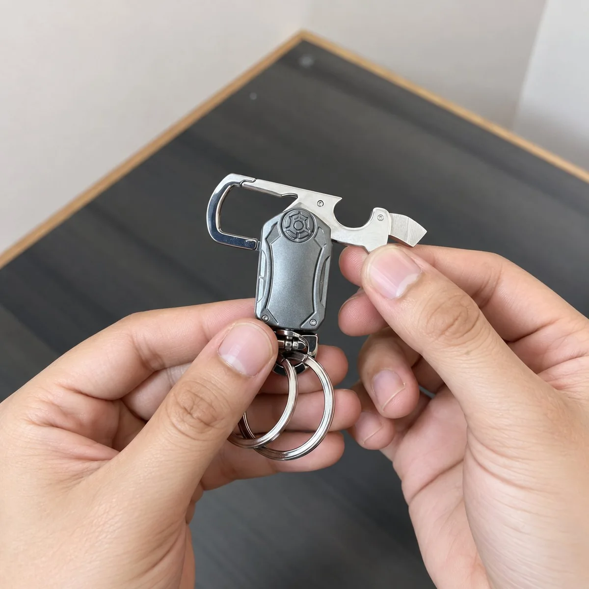 Two hands holding a compact metal multitool keychain — gray body with a small LED window