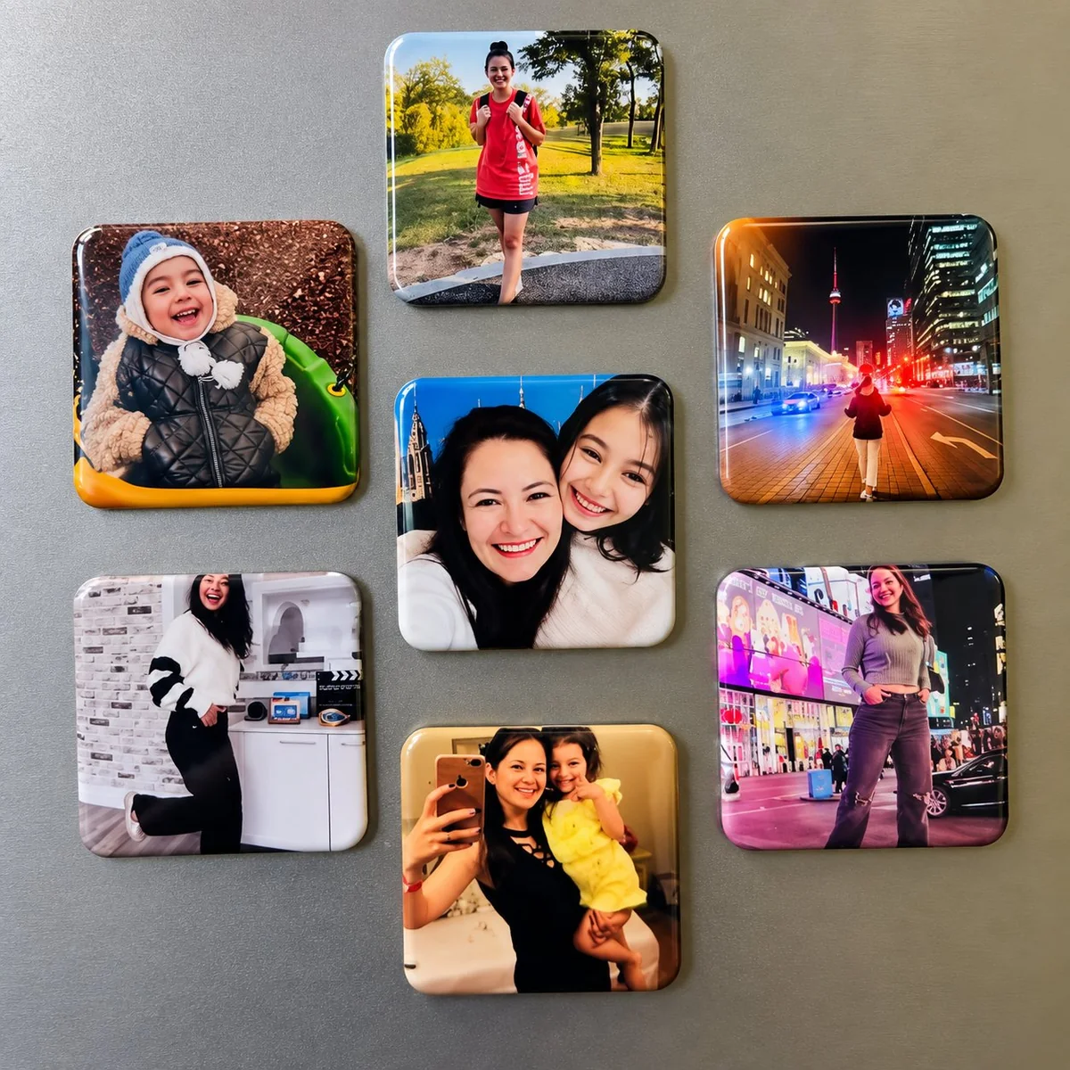 Seven photo fridge magnets arranged on a gray surface covering kids, family, travel and lifestyle subjects