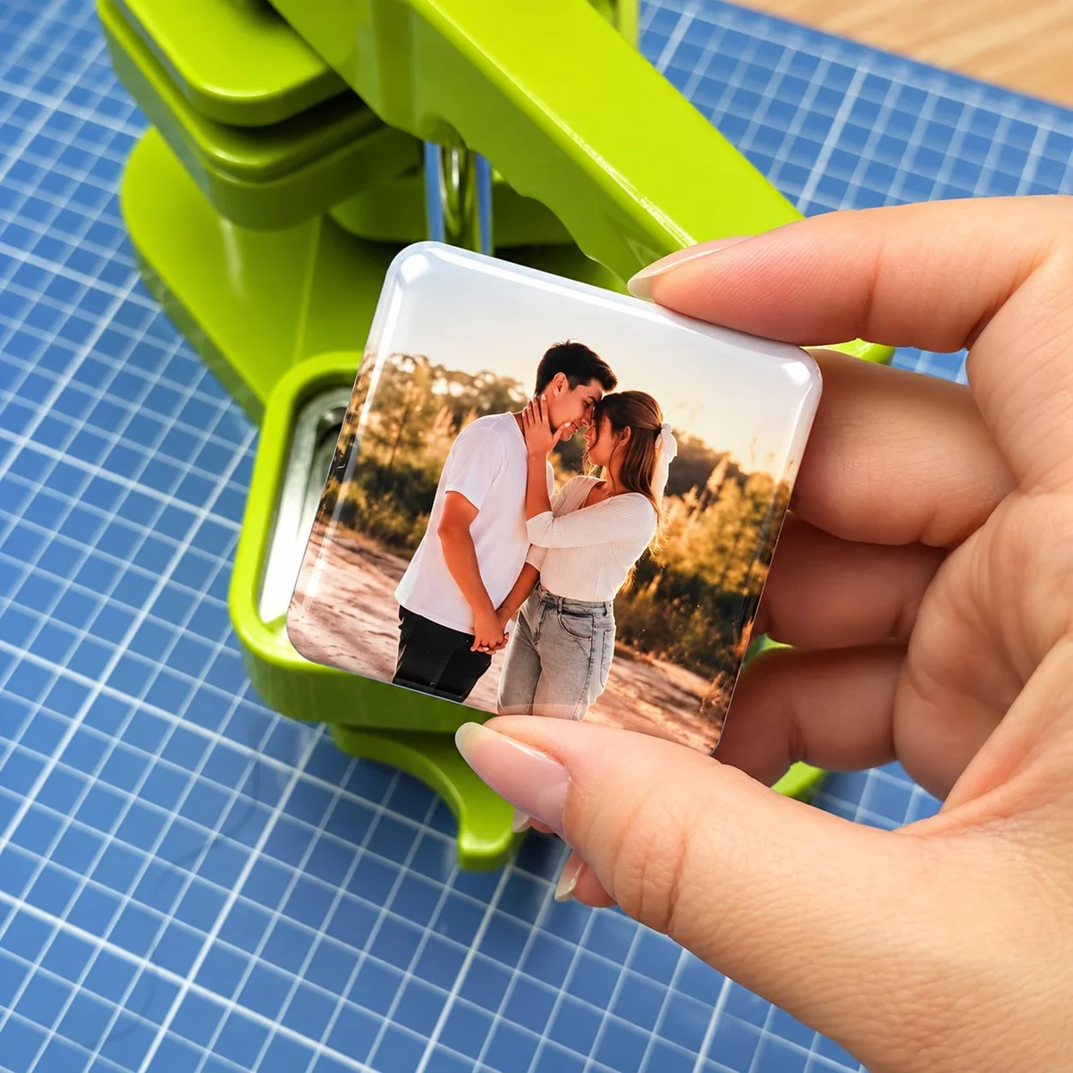 Hand holding a single square photo fridge magnet over a green die cutter on a blue cutting mat