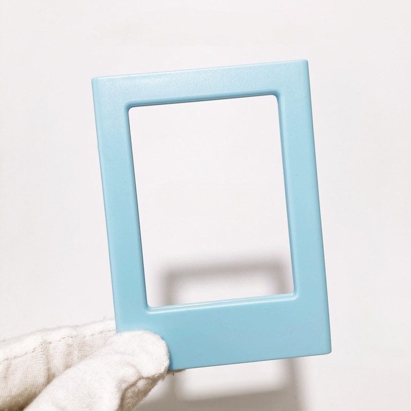 Magnetic picture frame in light blue held up in a gloved hand, showing the open window and the flat border
