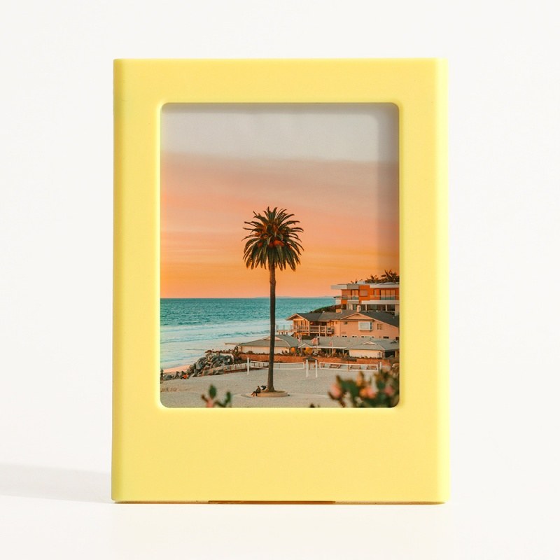 Magnetic picture frame in yellow holding a 3-inch instant photo, standing on a white surface