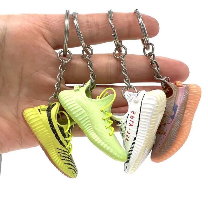 Yeezy shoe keychains on four coloured tag straps held on one hand, showing the strap and ring assembly