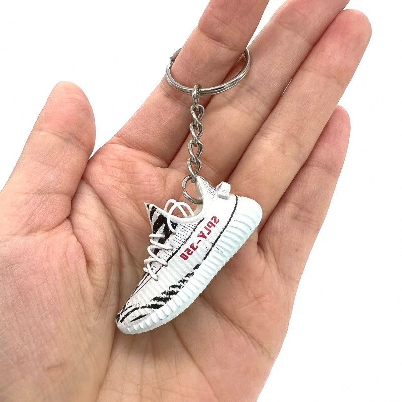 Yeezy shoe keychain in white PVC held in the palm, showing the knit-look upper and the ribbed sole