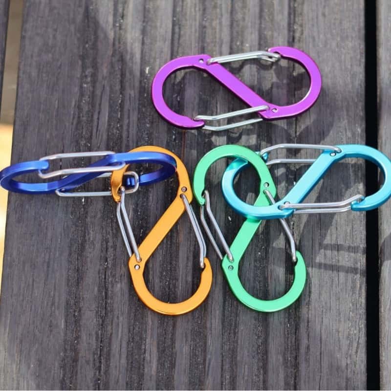 Aluminum carabiner keychains in five bright colors laid on a wooden deck