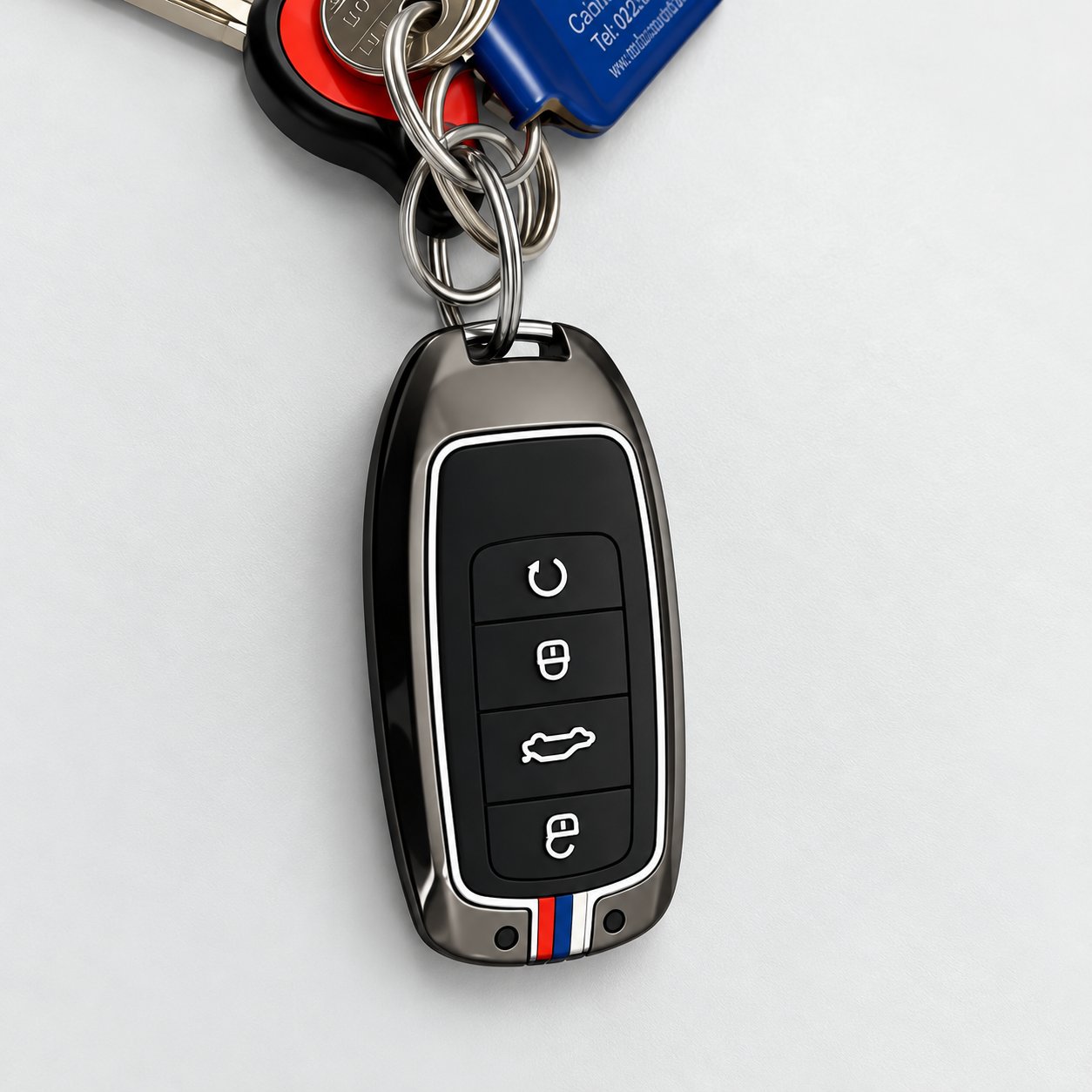 A close-up of a dark chrome key fob cover with four buttons and M-style blue, dark blue and red stripes on the base