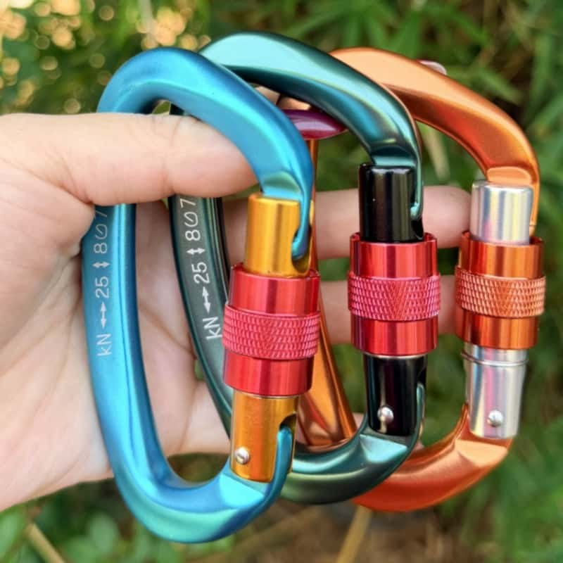Four anodized carabiner keychains held in one hand outdoors