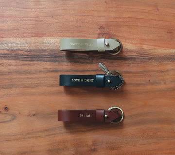 Three simple leather strap keychains arranged on a wooden background