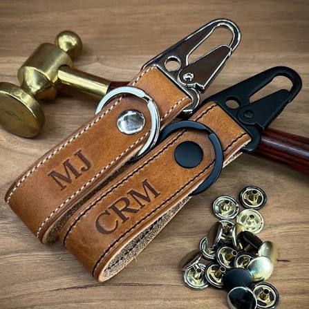 Personalized leather keychains with engraved initials on a wooden work surface