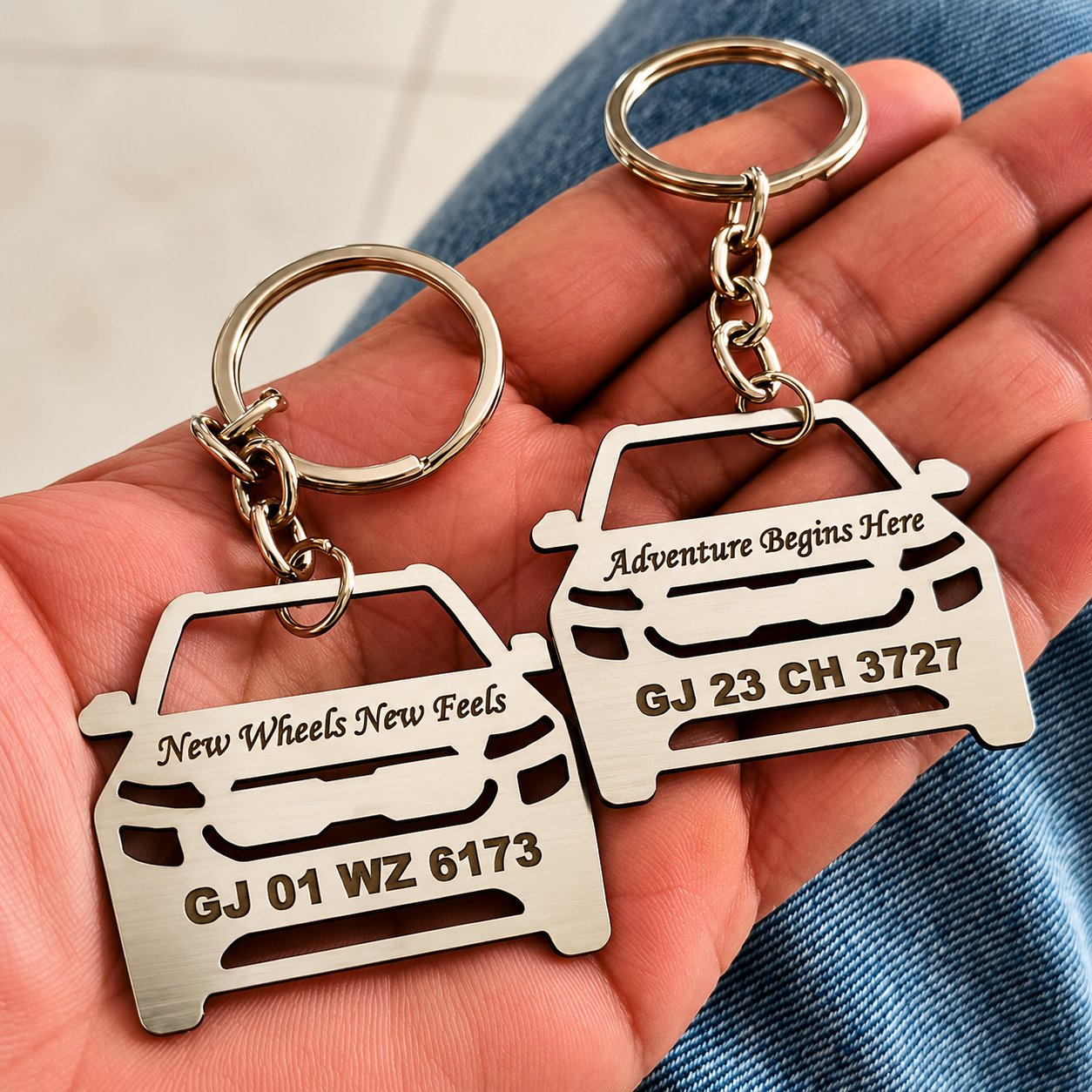 Two stainless steel car-shaped keychains held in a hand, laser-cut with engraved licence plate numbers and a custom message