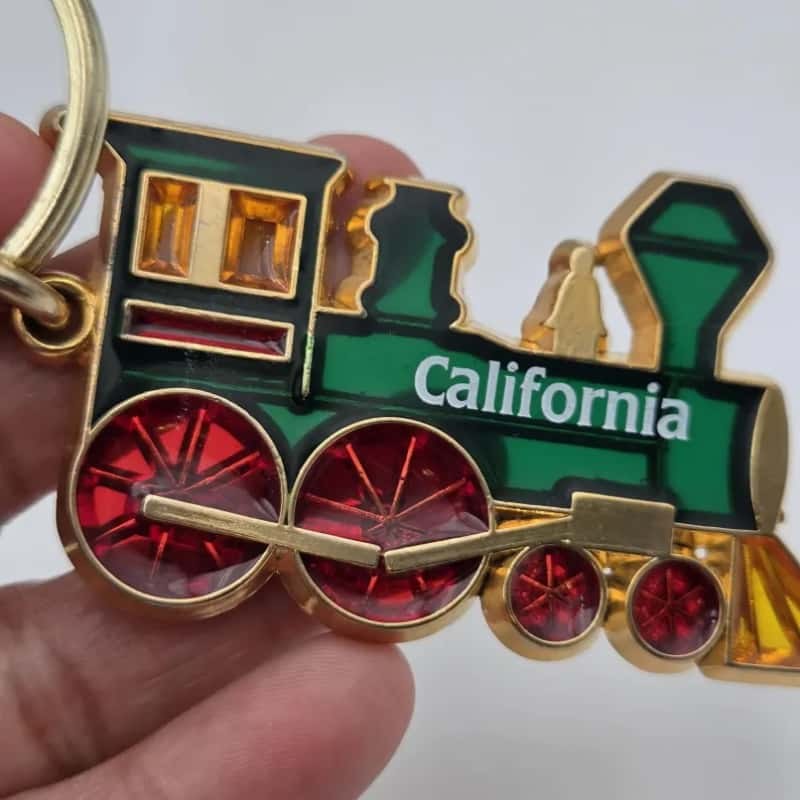 Hand holding the enamel train keychain to show its size and enamel colors