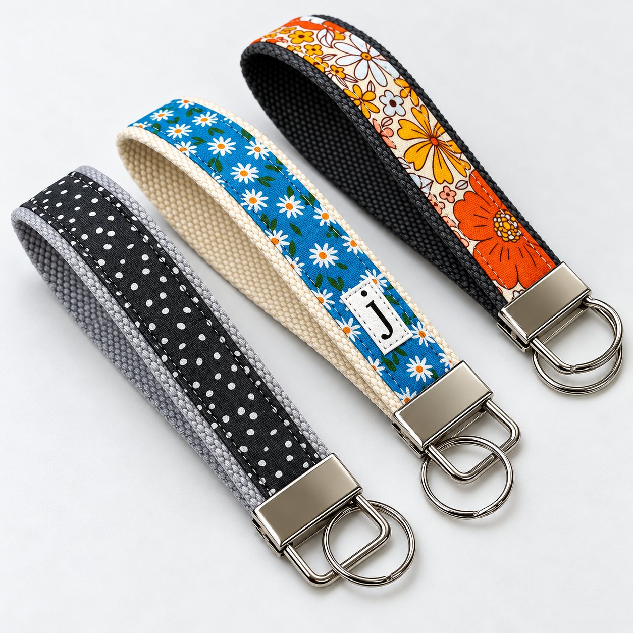 Three fabric wristlet keychain straps with metal hardware in black polka dot, blue daisy and orange floral patterns