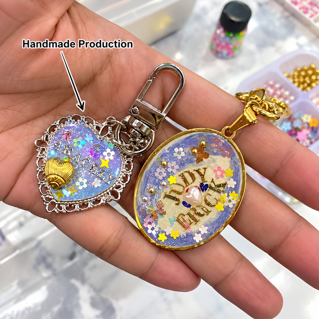 Two handmade resin keychains held in a hand, one heart shaped with a gold shell charm and one oval printed with a name and tulips.