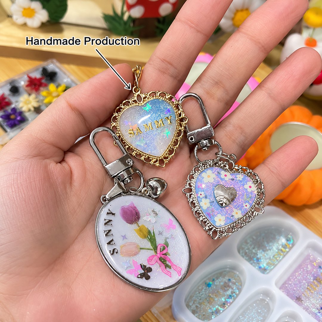 A handmade resin keychain with a gold filigree heart reading SAMMY beside an oval keychain printed with tulips and the name SANNA.