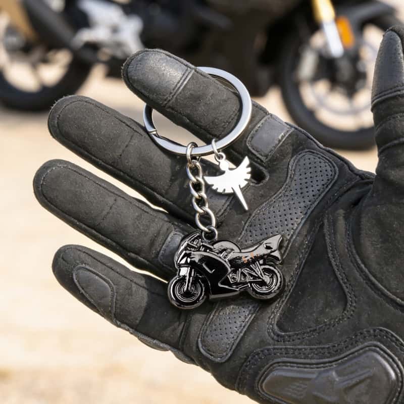 Motorcycle metal keychain held in a riding glove next to a parked bike