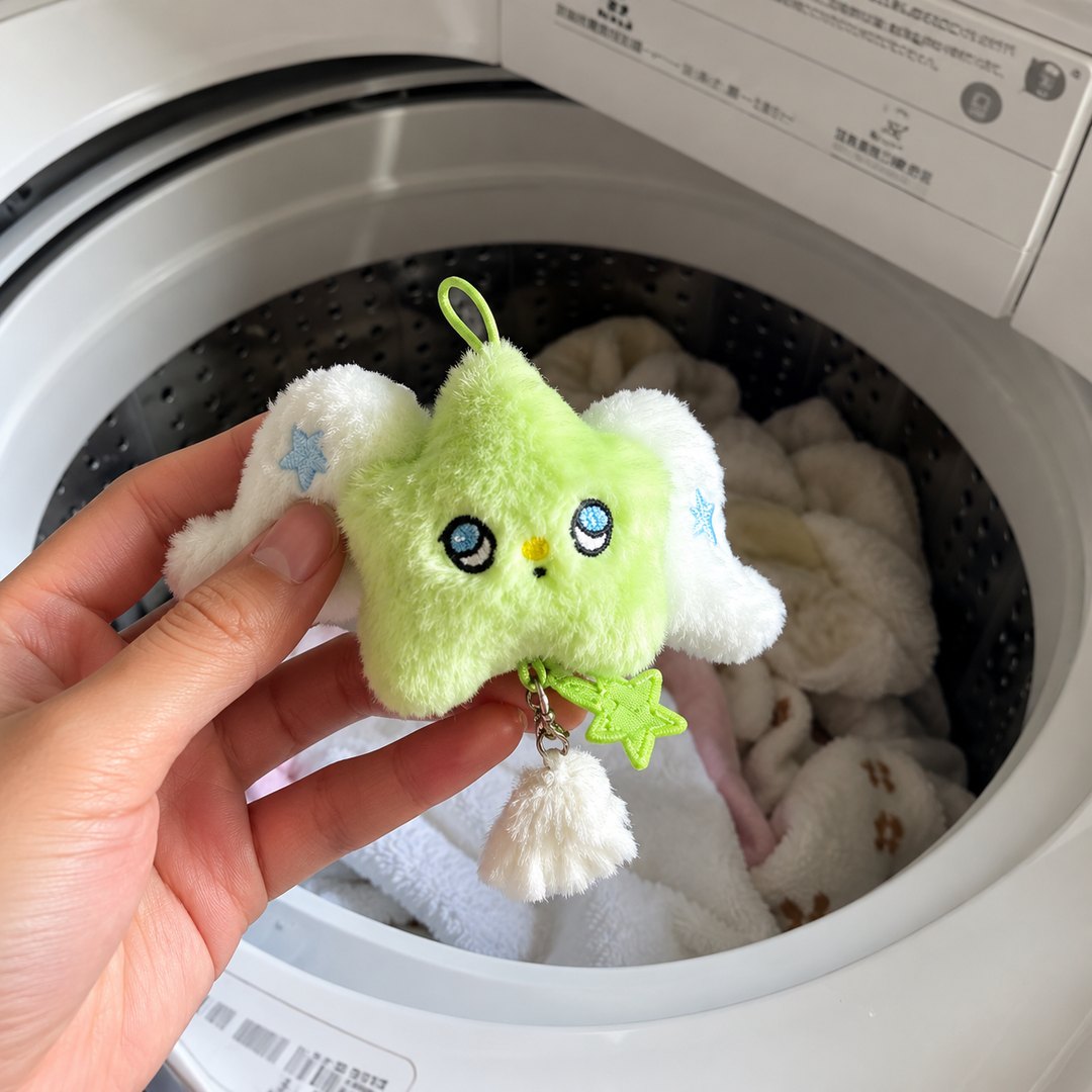 A green star plush keychain held in front of a washing machine drum, with a mesh laundry bag behind it.