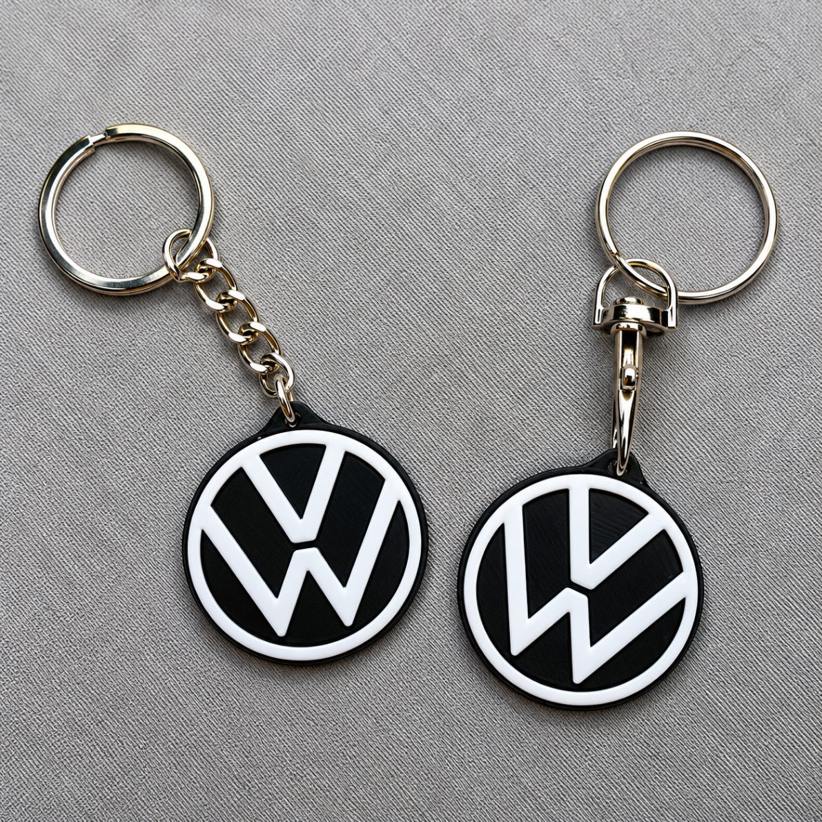 Two Volkswagen logo car keychains with black and white enamel on a grey background, one on a chain and one on a swivel connector