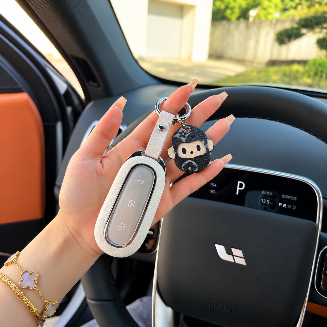 A hand holding a white leather car key fob cover with a cartoon monkey leather charm inside a car with an orange and black interior